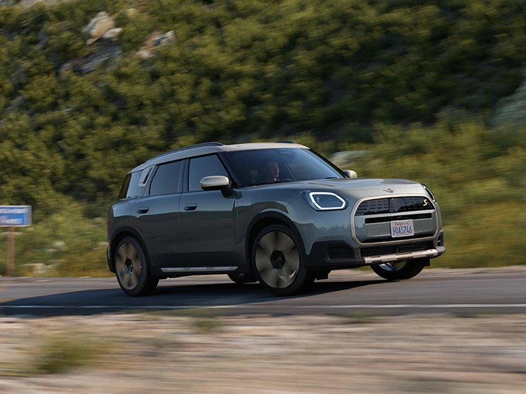 Side view of a driving all-electric MINI Countryman in Smokey Green with Vibrant Silver Roof offroad.